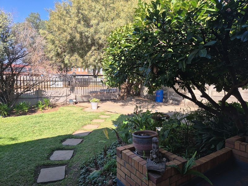 A private rear garden featuring a lawn, stone paver pathway, established trees, and a secure brick boundary wall with a metal gate.