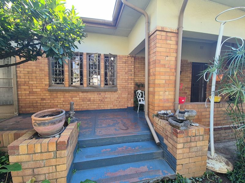A covered brick patio area featuring steps and built-in planter boxes, showing signs of wear on the painted surfaces.
