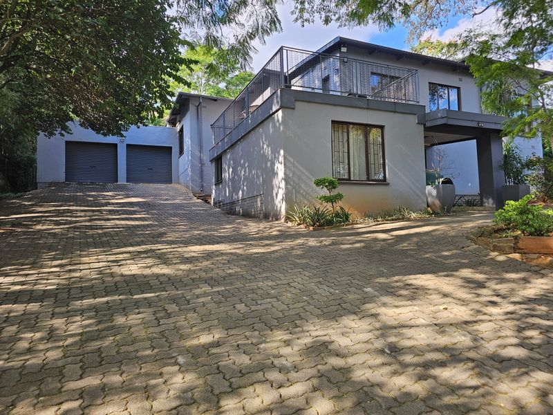 Front view of a modern double-story house featuring a paved driveway, double garage, and an upper-level balcony with metal railings.