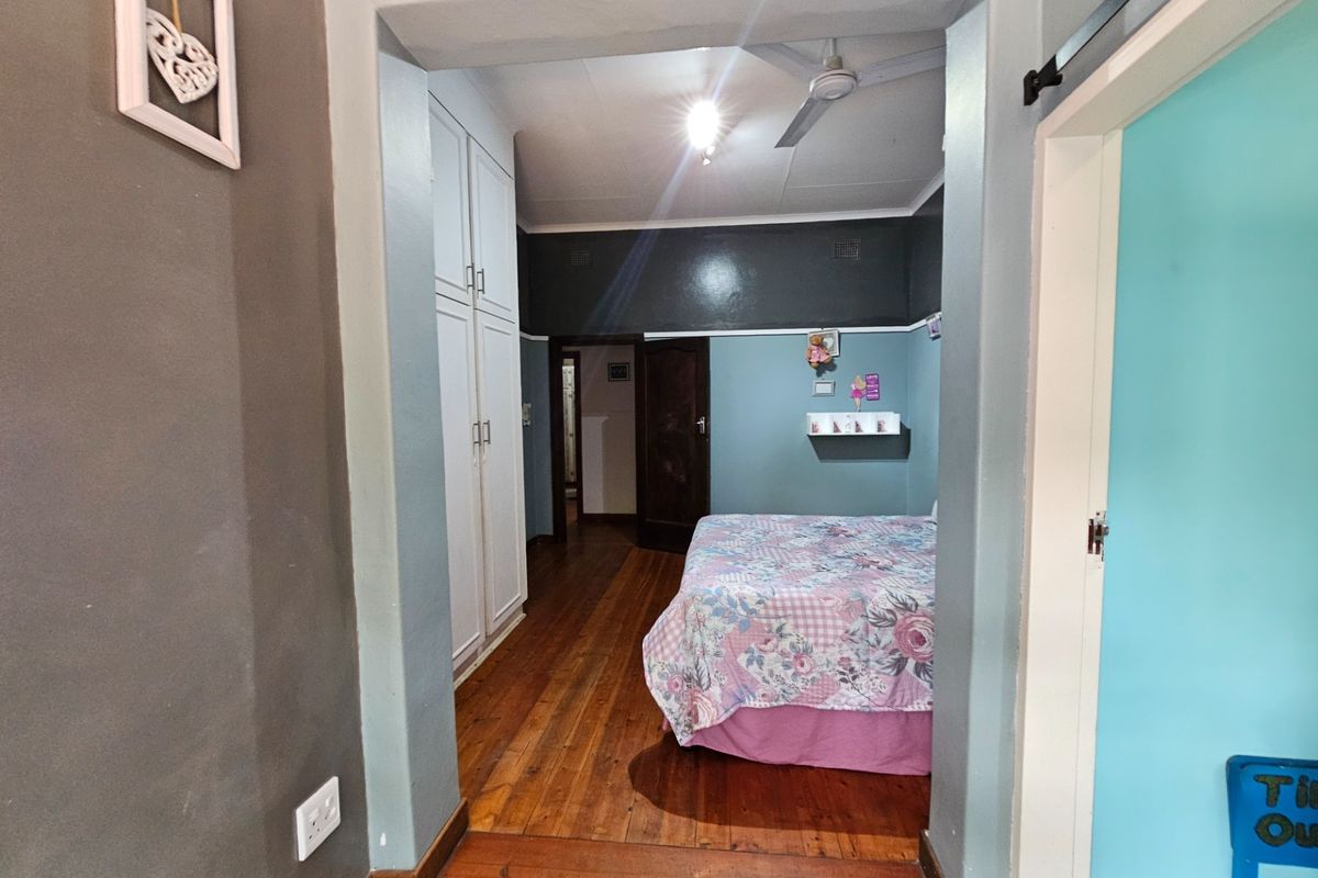 A bedroom featuring hardwood flooring, built-in cupboards, and a ceiling fan, viewed from an adjacent hallway.