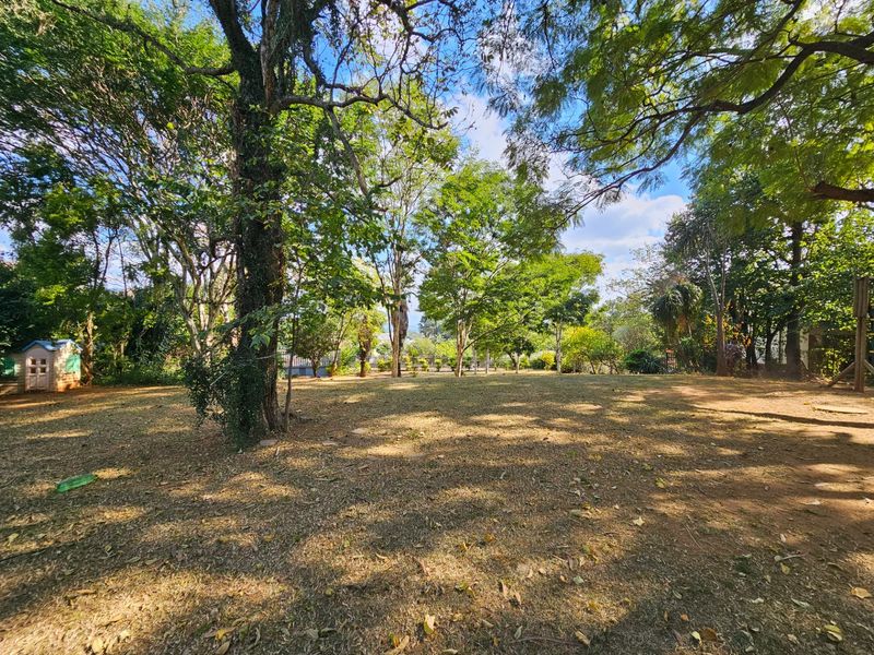 A spacious, tree-lined garden area featuring mature trees and established perimeter fencing, offering a private and natural outdoor setting.