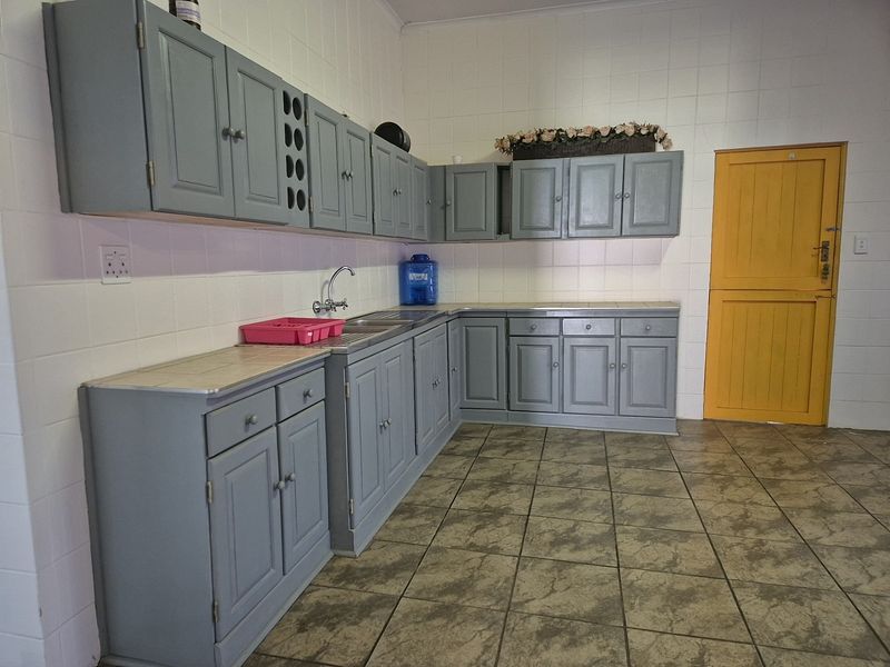 A functional kitchen featuring grey built-in cabinetry, tiled splashbacks, and tiled flooring, providing a clean and practical workspace.