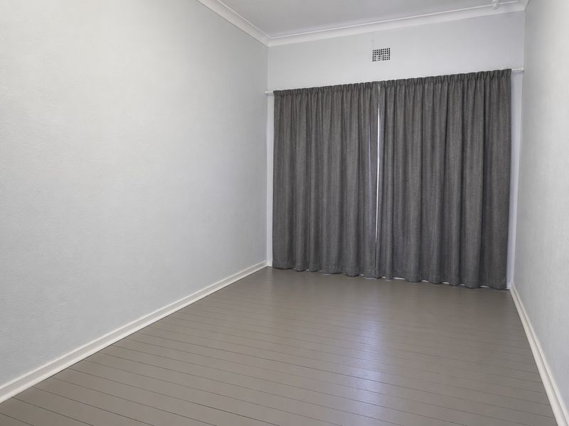 A clean, empty bedroom featuring neutral painted walls, timber flooring, and a ventilation grille, ready for staging or personal customization.