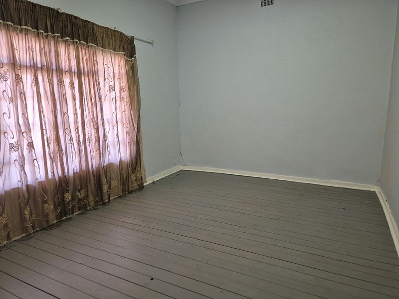 An empty bedroom featuring painted timber floorboards and neutral wall tones, providing a blank canvas for potential interior updates.