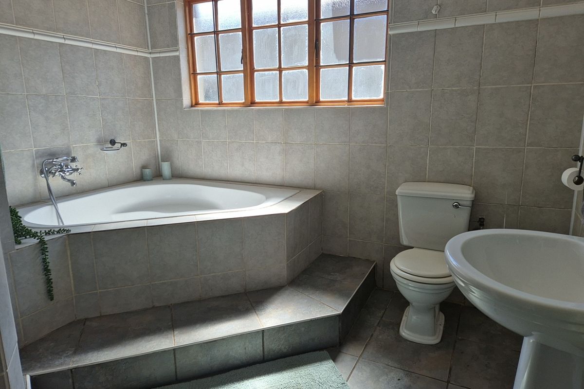 A functional bathroom featuring a corner bathtub, pedestal basin, and toilet with neutral wall and floor tiling.