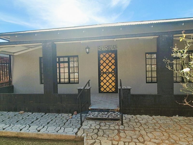 Front facade of the house featuring a covered porch, stone paved walkway, and secure metal entrance gate with decorative lattice design.
