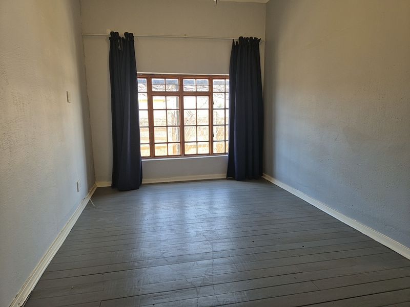 An empty bedroom featuring painted timber flooring, neutral walls, and a large timber-framed window with dark curtains.