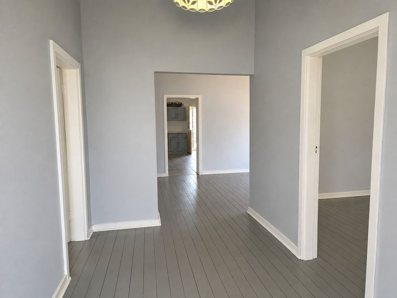 A bright and neutral hallway featuring painted timber flooring, clean lines, and multiple doorways leading into adjacent living spaces.