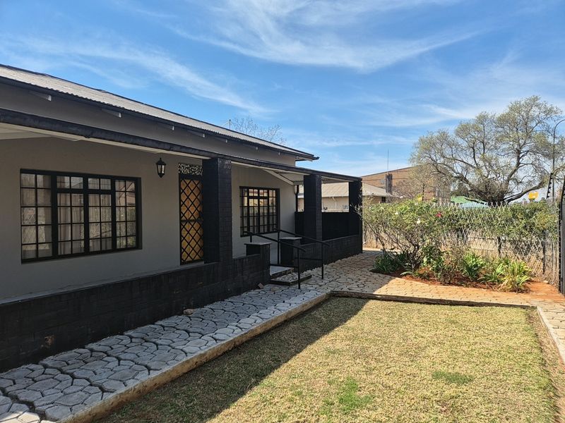A well-maintained rear exterior view featuring a covered patio, paved walkway, and landscaped garden area with secure fencing.