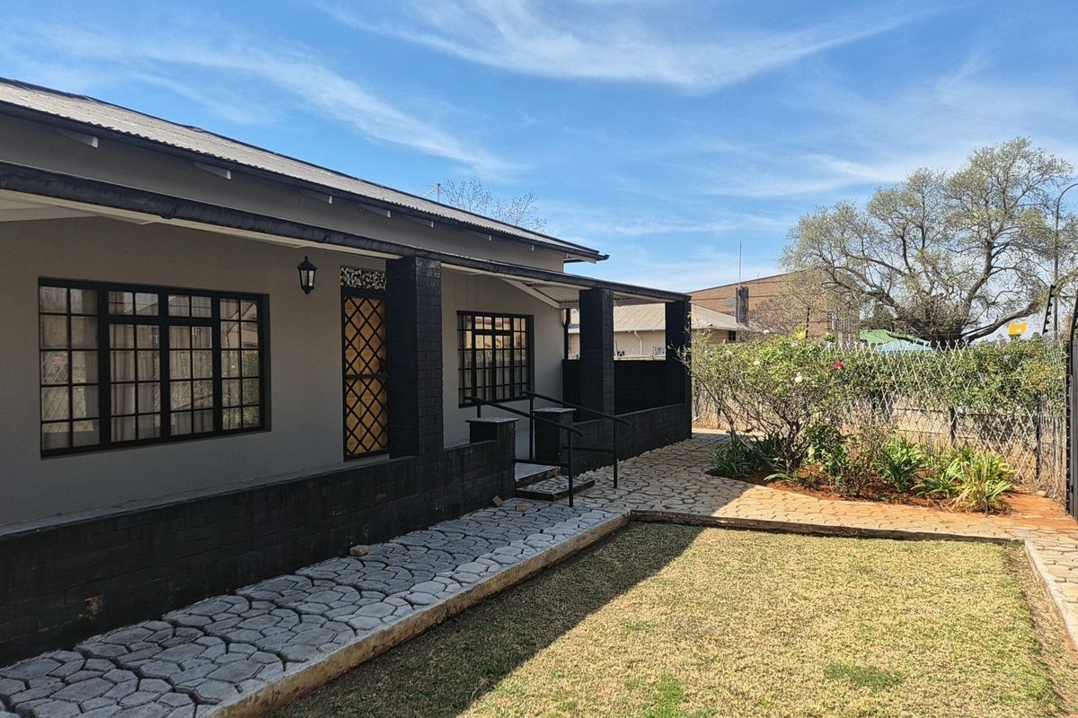 A well-maintained rear exterior view featuring a covered patio, paved walkway, and landscaped garden area with secure fencing.