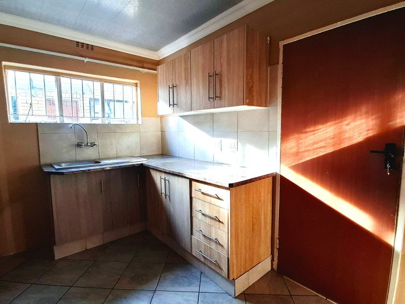 A functional kitchen featuring laminate cabinetry, tiled backsplash, and a stainless steel sink, offering a clean and practical layout for daily use.