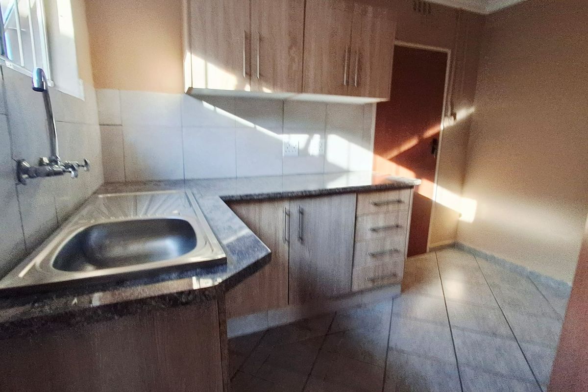 A functional kitchen featuring light wood-finish cabinetry, granite-look laminate countertops, a stainless steel sink, and tiled flooring.