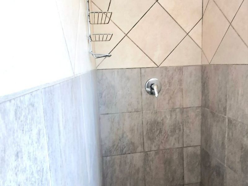 A functional shower enclosure featuring a mix of neutral-toned wall tiles and a tiled floor base with a standard shower mixer and head.