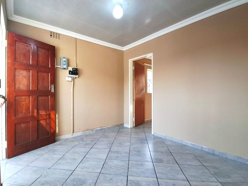 An empty living area featuring tiled flooring, neutral wall tones, and a wooden entrance door, providing a blank canvas for interior design.