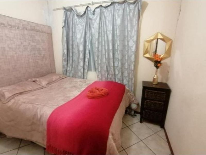 A standard bedroom featuring tiled flooring and a curtain rod, presented in a basic, lived-in condition.
