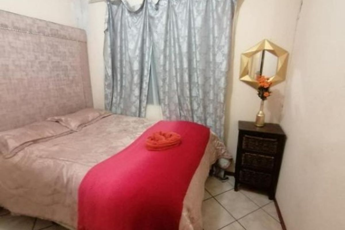 A standard bedroom featuring tiled flooring and a curtain rod, presented in a basic, lived-in condition.