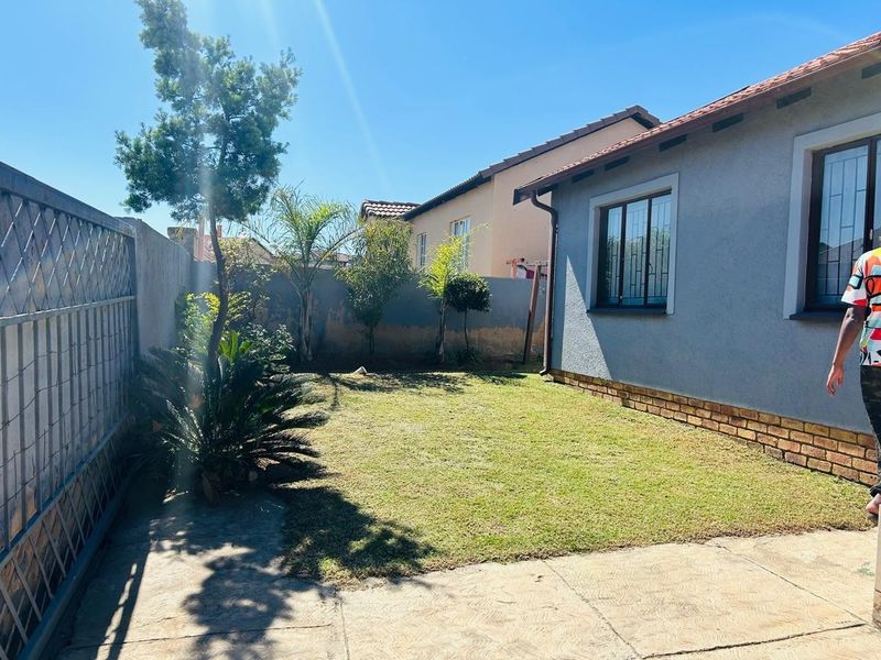 A private rear garden featuring a small lawn, paved patio area, and perimeter walling with security-fitted windows on the townhouse exterior.