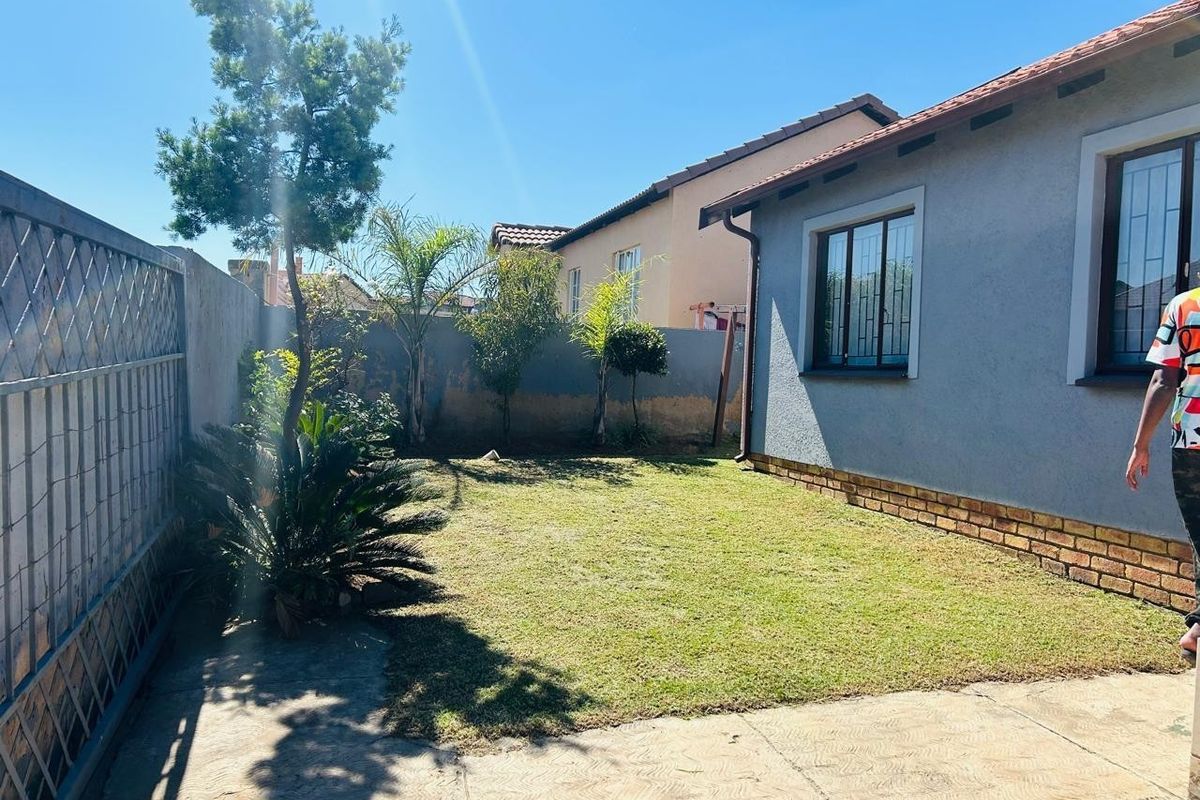 A private rear garden featuring a small lawn, paved patio area, and perimeter walling with security-fitted windows on the townhouse exterior.