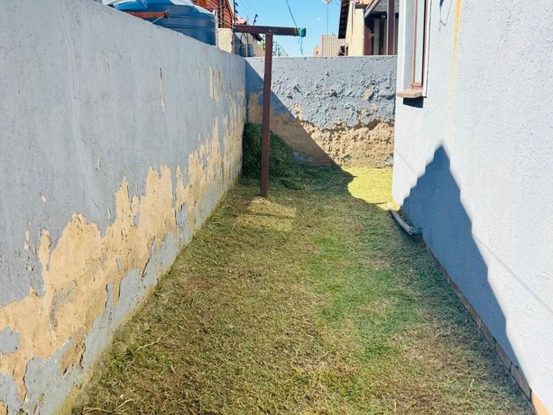 A narrow rear garden area featuring a boundary wall with visible paint and plaster deterioration, including a fixed washing line and water tank.