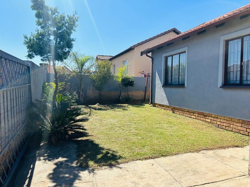 A private rear garden featuring a small lawn, paved patio area, and perimeter walling with security-fitted windows on the townhouse exterior.