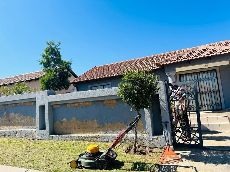 Front exterior view of a townhouse featuring a tiled roof, security gate, and a perimeter wall requiring maintenance and repainting.