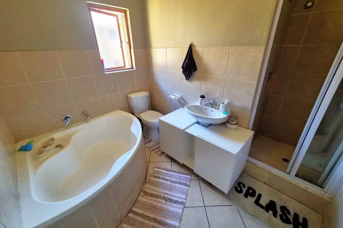A functional bathroom featuring a built-in corner bathtub, a separate shower enclosure, a toilet, and a vanity basin with tiled finishes.