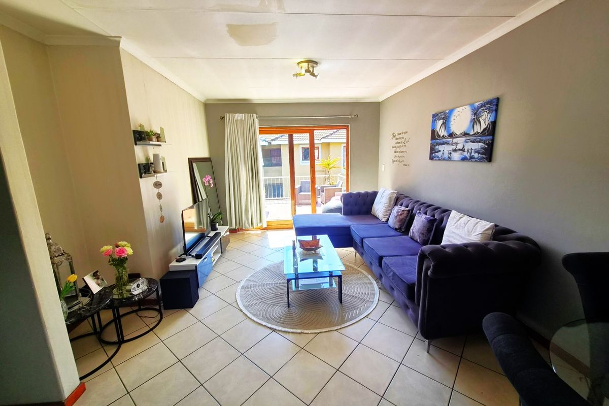 A living room featuring tiled flooring and a sliding glass door leading to a balcony, with a visible water stain on the ceiling.