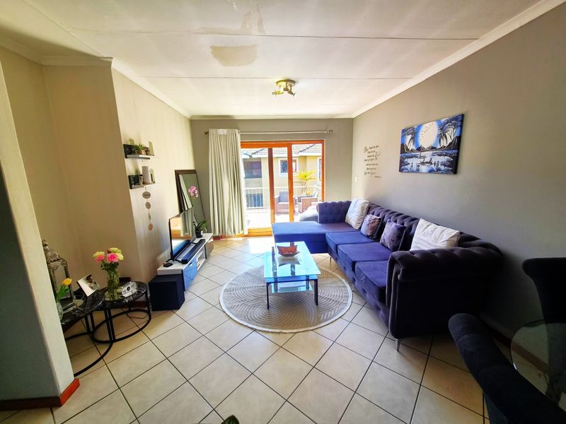 A living room featuring tiled flooring and a sliding glass door leading to a balcony, with a visible water stain on the ceiling.