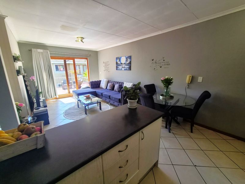 Open plan living and dining area featuring tiled flooring, kitchen cabinetry with dark countertops, and a sliding door leading to an outdoor balcony.