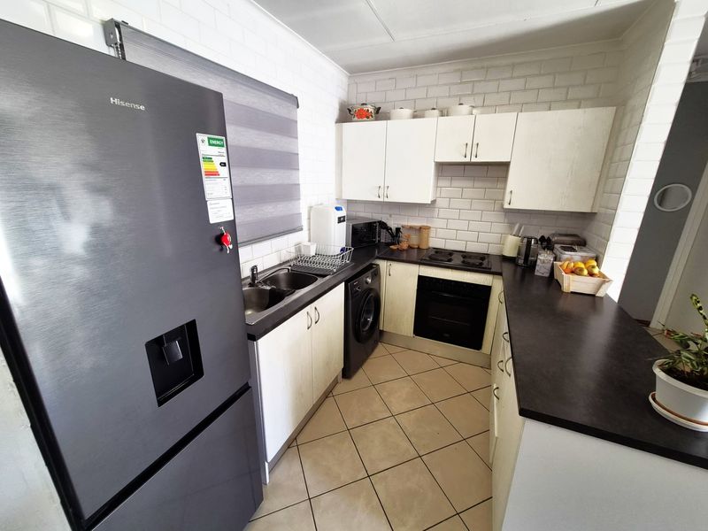 A functional kitchen featuring white cabinetry, dark laminate countertops, tiled backsplash, built-in oven, electric hob, and tiled flooring.