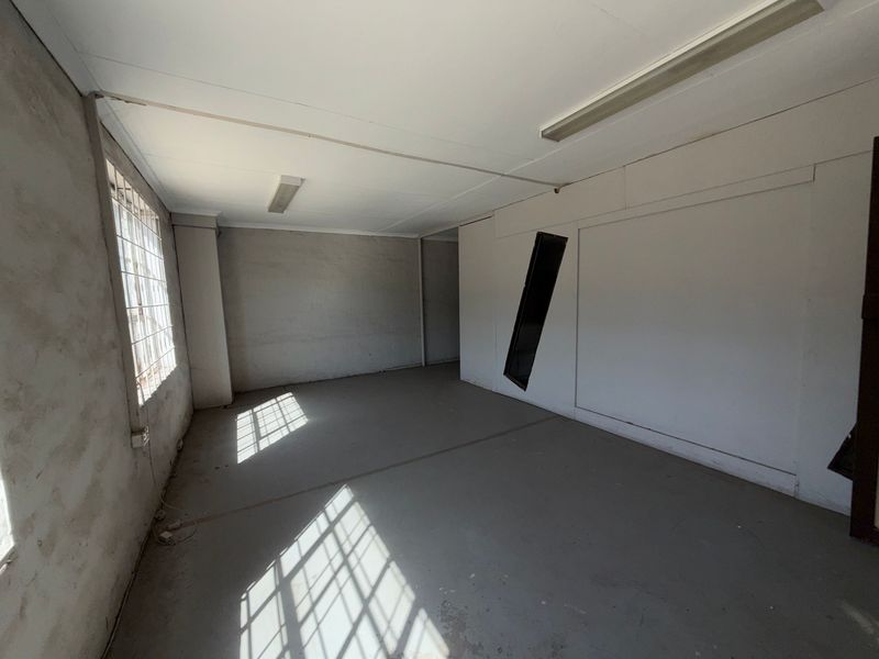 An empty industrial utility space featuring concrete flooring, fluorescent lighting, and security-barred windows, suitable for storage or workshop use.