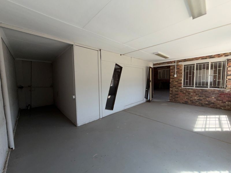 An empty industrial utility space featuring exposed brickwork, concrete flooring, and security bars on the windows, suitable for storage or workshop use.