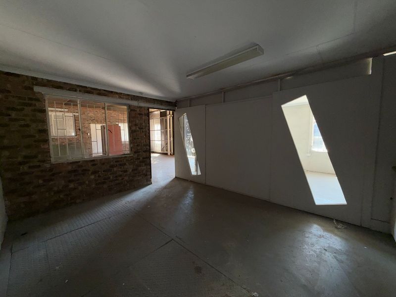 An empty industrial office space featuring exposed brickwork, concrete flooring, and unique geometric partition wall cutouts, offering a versatile layout for commercial use.