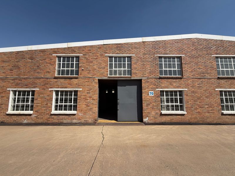 Front elevation of an industrial warehouse featuring exposed brickwork, multiple steel-framed windows, and a large central access door with a concrete apron.