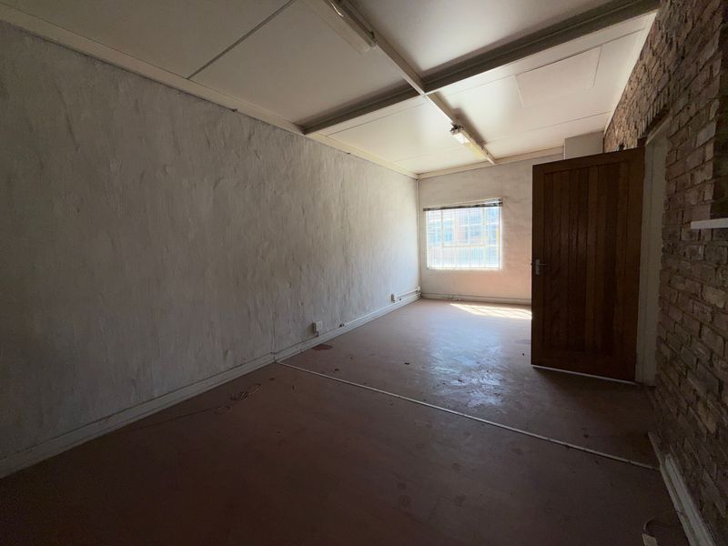 An empty industrial-style office space featuring exposed brickwork, a timber door, and fluorescent lighting, offering a blank canvas for renovation.