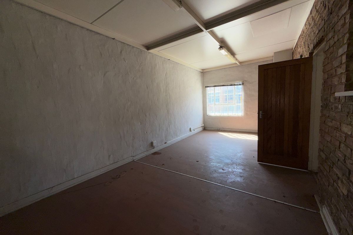 An empty industrial-style office space featuring exposed brickwork, a timber door, and fluorescent lighting, offering a blank canvas for renovation.