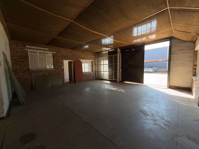 Spacious industrial utility area featuring exposed brick walls, concrete flooring, and a large sliding access door, suitable for workshop or storage use.