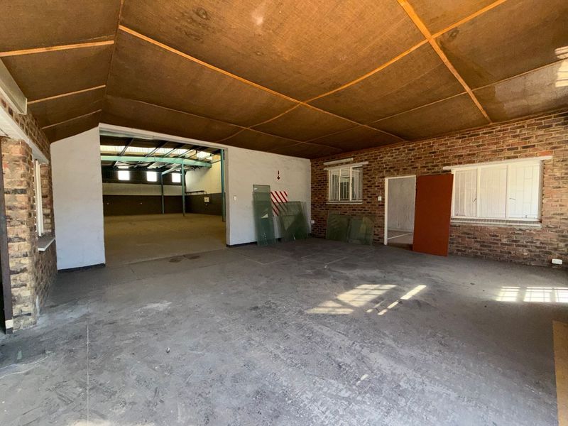 Spacious industrial utility area featuring exposed brick walls, concrete flooring, and a timber panel ceiling, offering versatile space for storage or workshop use.