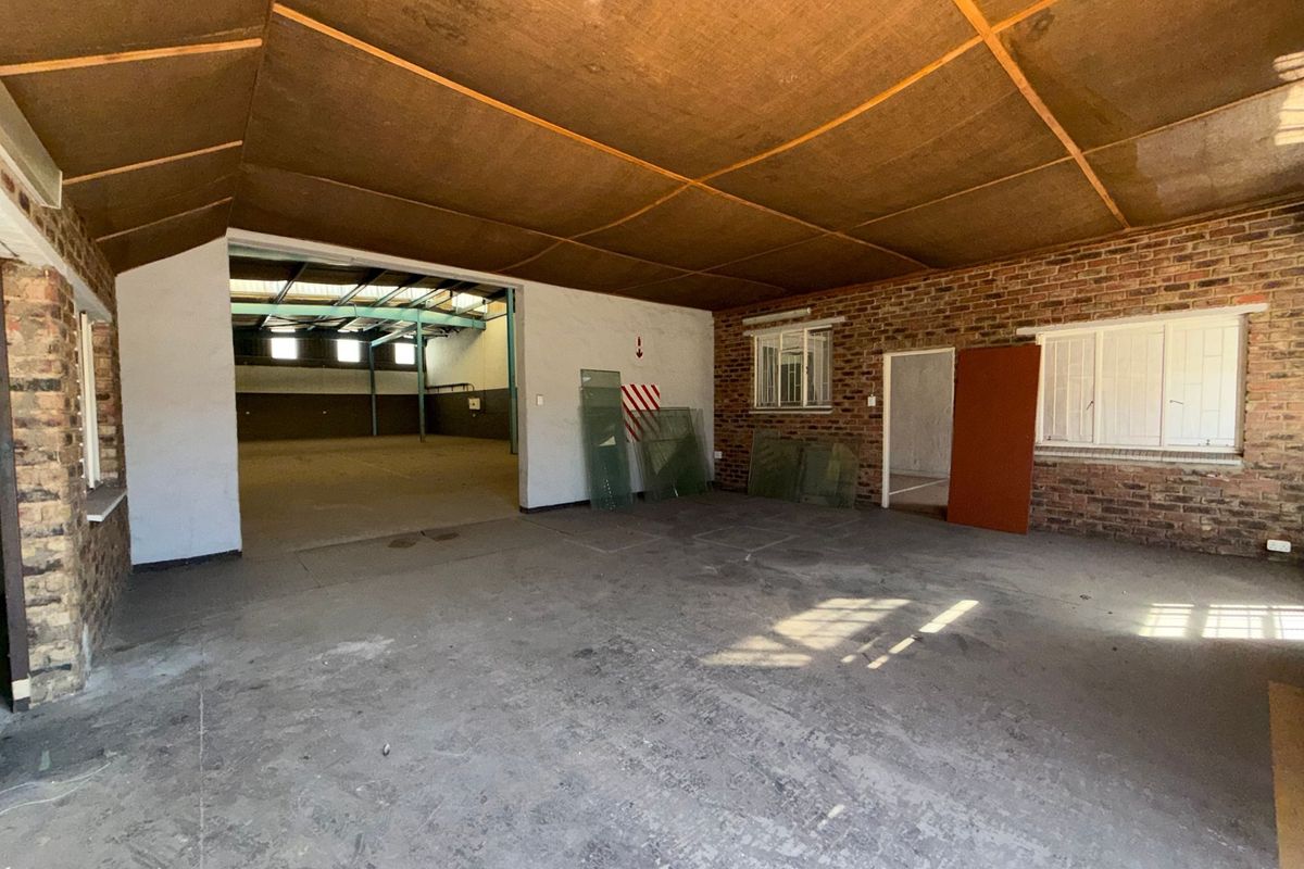 Spacious industrial utility area featuring exposed brick walls, concrete flooring, and a timber panel ceiling, offering versatile space for storage or workshop use.
