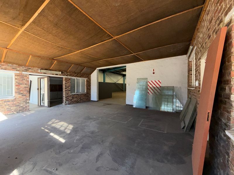 Spacious industrial utility area featuring exposed brick walls, concrete flooring, and a suspended ceiling, suitable for storage or workshop use.