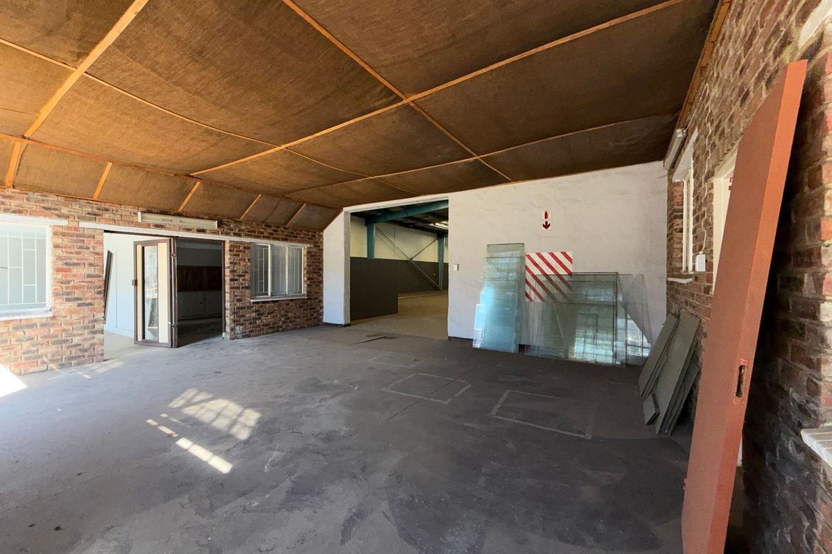 Spacious industrial utility area featuring exposed brick walls, concrete flooring, and a suspended ceiling, suitable for storage or workshop use.