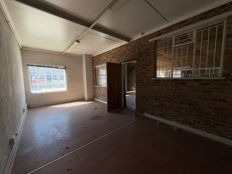 An empty industrial office space featuring exposed brick walls, security-barred windows, and functional fluorescent lighting, suitable for renovation or commercial fit-out.