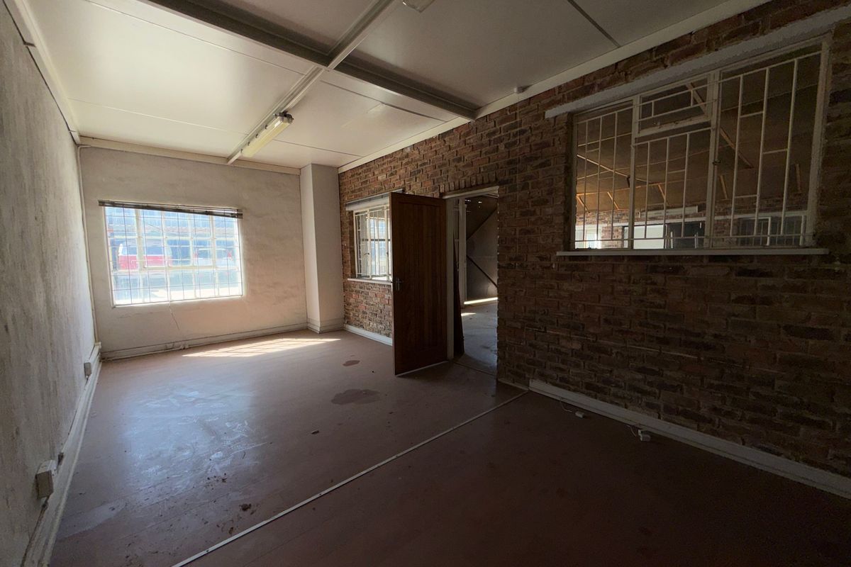 An empty industrial office space featuring exposed brick walls, security-barred windows, and functional fluorescent lighting, suitable for renovation or commercial fit-out.