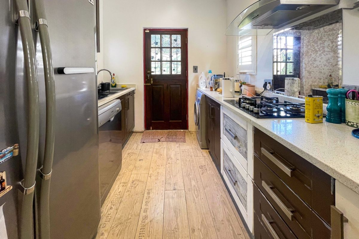 A functional galley-style kitchen featuring dark cabinetry, stone countertops, a gas hob with extractor fan, and durable timber-look tile flooring.