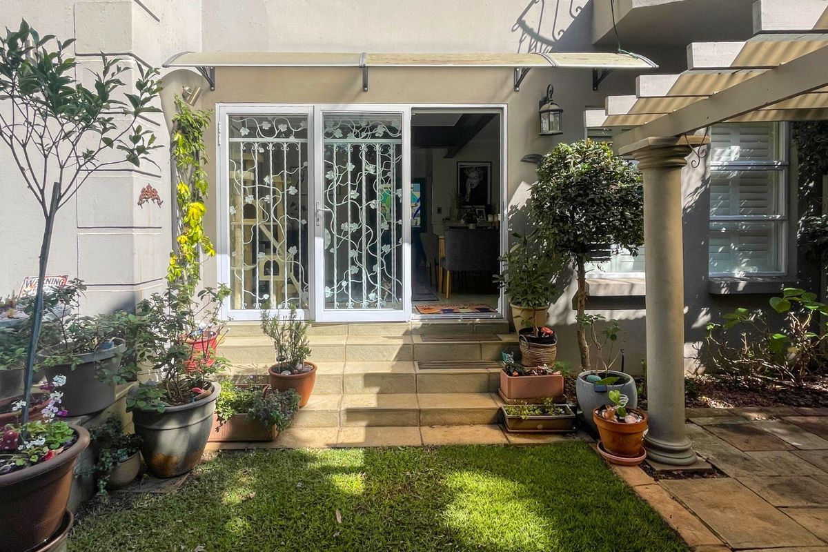 A rear exterior view featuring a tiled patio area, a decorative security gate, and a covered entrance leading into the home.