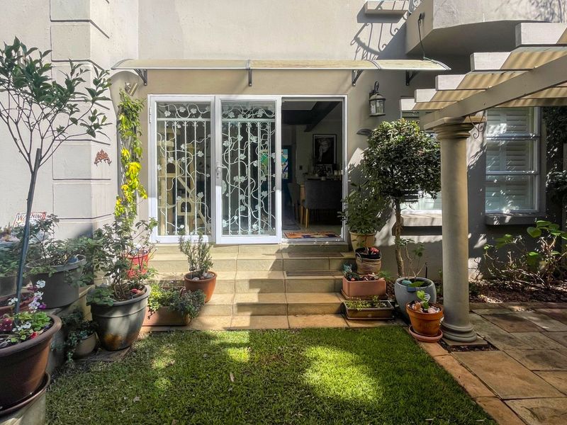 A rear exterior view featuring a tiled patio area, a decorative security gate, and a covered entrance leading into the home.