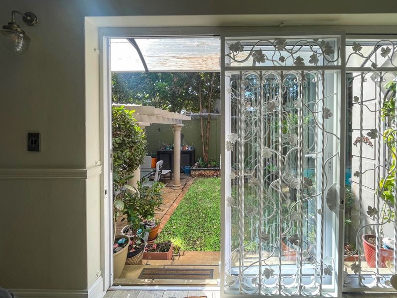 View from an interior space through a decorative security gate and sliding door onto a paved patio area with a pergola and garden.