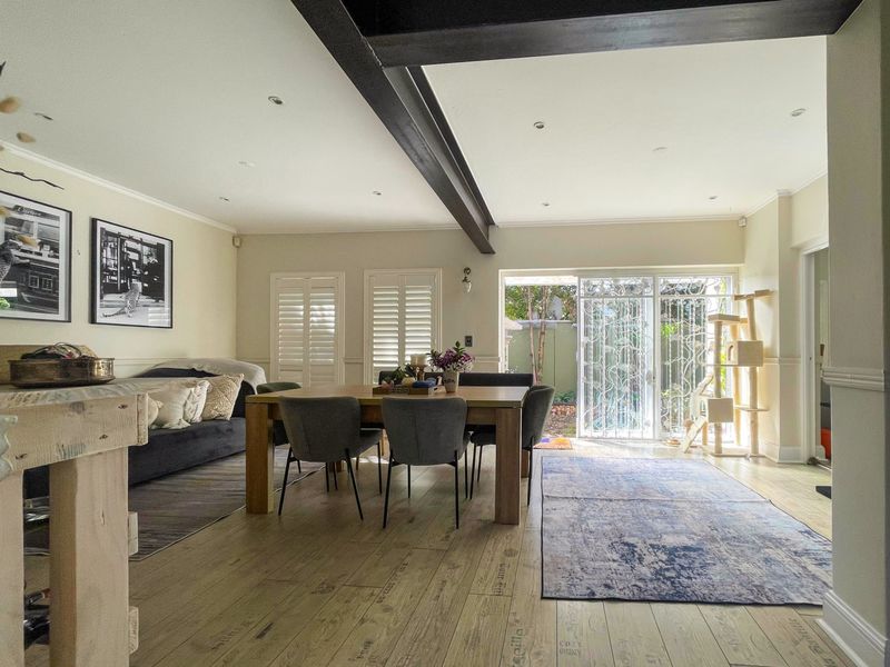 Spacious open-plan living and dining area featuring exposed ceiling beams, plantation shutters, and direct access to the rear garden through sliding glass doors.