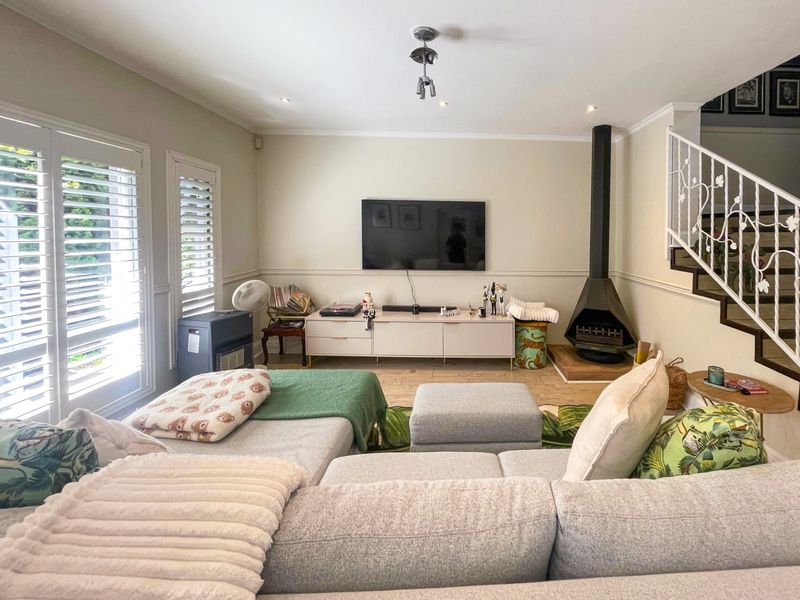 A comfortable living room featuring a modern freestanding fireplace, plantation shutters, and an elegant staircase with a decorative metal balustrade.