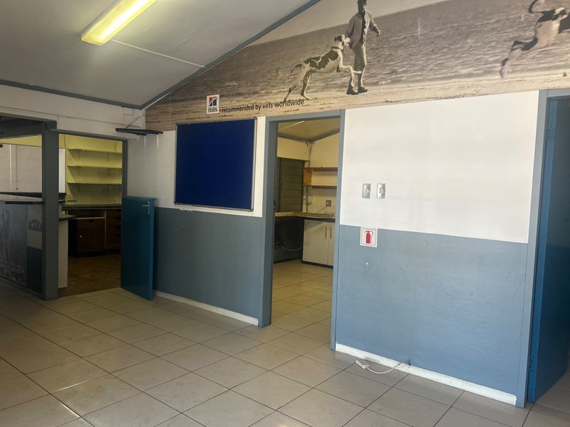 An open-plan office space featuring tiled flooring, fluorescent lighting, and multiple partitioned work areas with built-in cabinetry.
